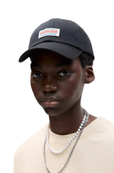 Gorra negra estilo mecánico para hombre con la palabra “L’atelier” bordada en negro y ubicada encima de un cuadrado blanco. Incluye el modelo