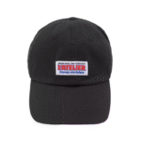 Gorra negra estilo mecánico para hombre con la palabra “L’atelier” bordada en negro y ubicada encima de un cuadrado blanco. Incluye el modelo