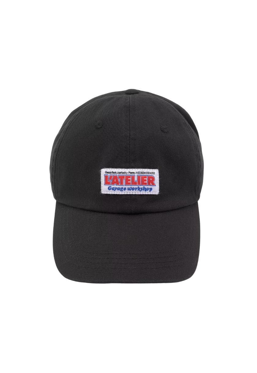 Gorra negra estilo mecánico para hombre con la palabra “L’atelier” bordada en negro y ubicada encima de un cuadrado blanco. Incluye el modelo